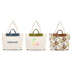 Three canvas bags with leather handles in cream, featuring different designs: text, a colourful symbol, and floral patterns.