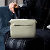 A soft-touch toiletry bag in light cream, positioned on a suitcase, with two handles visible.