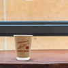 A kraft paper cup with a double wall design, featuring a red logo and sitting on a wooden surface.