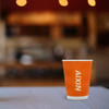 An orange disposable corrugated double wall paper cup with a logo, set against a blurred café background.