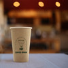 A disposable single wall kraft paper cup in a natural brown colour with a logo. Background features a cafe setting.