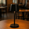 A black mini rechargeable lamp with a tapered shade, standing on a circular base, placed on a wooden table.