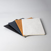 A set of four notebooks in black, navy, brown, and white, featuring smooth covers and a clean design.