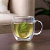 A double wall mug made of clear glass, containing green tea with a handle. It features a logo on the front.