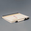 A spiral-bound notebook in cream with a black pen resting on it, featuring a logo on the cover.