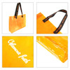 A clear tote bag in bright orange with black handles featuring a logo. The bag has a glossy finish.