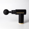 A black massage gun with a gold base and a round black attachment, featuring a sleek design and a logo.