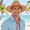 A natural straw hat with a wide brim and red detailing, worn by a man on a beach.
