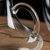 A clear glass decanter featuring a unique handle design, resting on a wooden surface.