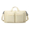 A foldable travel duffle bag in cream with two front pockets and a detachable shoulder strap. Features a logo.