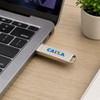 A silver double-end swivel Type C flash drive plugged into a laptop, with a small plant and notebook in the background.