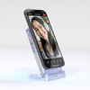 A clear acrylic wireless charging stand displaying a smartphone in a vertical position, featuring a smiling face on the screen.