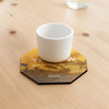 An octagonal frosted metal coaster in yellow and black, featuring a white cup placed on top.