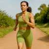 A woman runs on a dirt path wearing green high-waisted elastic yoga 1/2 leggings and a matching crop top.