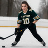 A young woman wearing a green and yellow retro V-neck hockey jersey, poised with a hockey stick on an ice rink.