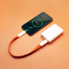 A white power bank connected to a smartphone with an orange charging cable. The phone displays a battery charging symbol.