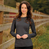 A woman models a long-sleeve, charcoal grey tee with a simple design, set against a natural outdoor backdrop.