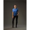 A woman stands wearing a blue Women's Reflex Polo shirt paired with black pants in a studio setting.