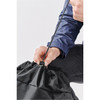 A black backpack with a drawstring closure being pulled tight by a hand. The material appears durable and lightweight.