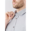 A close-up of a man adjusting the collar of a light grey button-up shirt with a pocket and buttons.