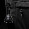 A black laptop sleeve features a textured surface and a keychain with a small black character.