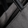 A grey tote bag featuring dark green leather handles and stitching, with a close-up view of the fabric texture.