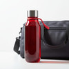 A drink bottle in a vibrant red colour with a silver lid and a handle, positioned next to a grey bag.
