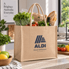 A tan Juco bag with two handles, filled with fresh produce, bread, and a bottle. It features a logo on the front.