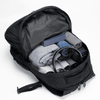 A black backpack with neatly arranged rolled clothes, a box, and a pair of headphones inside.