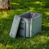 A grey cooler box with a detachable lid, positioned on grass, surrounded by outdoor scenery.