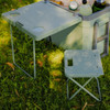 A green cooler box with a table and a small folding chair, placed on grass, featuring drink holders.