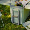 A grey cooler box filled with drinks and ice, accompanied by small folding chairs on green grass.