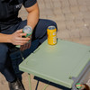 A green cooler box with a foldable table and chair, featuring two drink cans on the table.