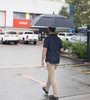 A person walking under a large black golf umbrella, with cars and a post office in the background.