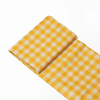 A yellow and white checked picnic blanket folded neatly, featuring a slight sheen and a compact design.