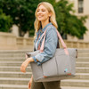 A grey foldable sports duffle bag with pink straps, carried by a smiling woman outdoors. It features a logo.