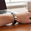 A stainless steel buckle latch bracelet in black worn on a wrist, with a laptop and cup in the background.