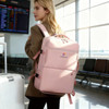 A pink expandable travel backpack with a logo, worn by a person in a transit area alongside a suitcase.