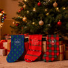 Three Christmas stockings hang in front of a decorated tree, featuring blue, red, and patterned designs.
