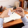 A hand holds glasses and a small white pouch, with books and stationery visible on a wooden desk.