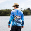 A man wearing a blue long sleeve polyester fishing tee with a fish graphic, standing by a body of water.