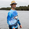 A man wearing a long sleeve blue polyester fishing tee, featuring a fish graphic, near a body of water.