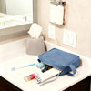 A toiletry bag with a handle in blue, placed on a countertop with various personal care items beside it.
