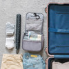 A grey hanging travel toiletry bag with compartments and contents, alongside folded clothes and an umbrella.