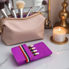 A bright purple travel organiser with essential oil vials, next to a beige makeup bag and a lit candle.