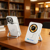 A white 10000mAh magnetic wireless power bank with a phone stand, on a wooden table in a library setting.