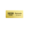 A metal name badge in a gold finish, featuring black text with a logo on one side.