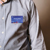 A person wearing a checkered shirt with a blue custom PVC name badge attached. The badge features a logo.