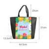 A tote bag with a full-colour tropical design featuring fruits, flowers, and a parrot, plus a black base and handles.