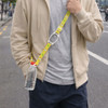 A drink bottle with a bright yellow lanyard is held by a person wearing a beige hoodie in an outdoor setting.